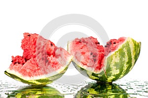 Watermelon halves pieces with cracks and water drops on white mirror background with reflection isolated close up