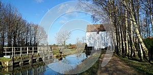 Watermill and Mill stream at Lode in Cambridgeshire with trees and blue sky.