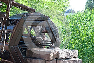 Watermill wooden water wheel mill, stone bricks wall, water flows from the wheel, on the background of green trees