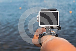 Waterproof action camera with mounts on a man`s hand. Against the backdrop of the blue water of the sea