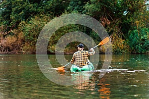 Watersport. Man in shirt and cap kayaking at the river. Back view. The concept of the World Tourism Day