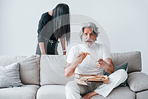 Wathing TV with scary woman with black hair near him. Senior stylish modern man with grey hair and beard indoors