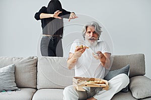 Wathing TV with scary woman with black hair near him. Senior stylish modern man with grey hair and beard indoors
