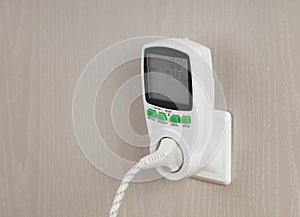 Wattmeter for measuring electricity costs with plug connected to the outlet, in socket on wall