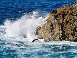 Wave action onto rocky outcrop. Blue seas, white wave orange rock