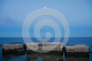 Wave breakers in harbor of Marzamemi, Sicily, at sunset with full moon.