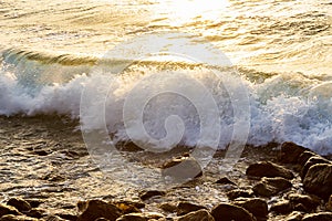 Wave breaking on rocks at shoreline with sunrise