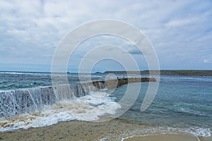 Wave breaking on Sennen cove fishing harbor breakwater