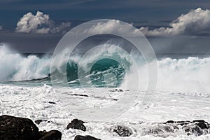 Wave breaking on western Kona coast in Hawaii. White spray and foam on the water. Rocks in foreground.