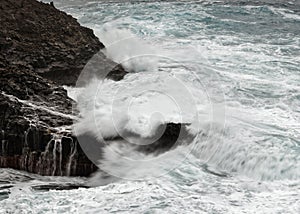 A wave breaks in stormy weather on a rocky coast