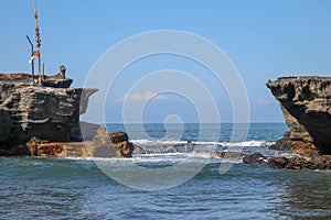 Wave crashing onshore at low tide in Bali, Indonesia. Water cascading over stone, feeding tidal pool. Wave breaking on rock during