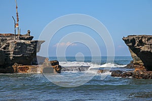 Wave crashing onshore at low tide in Bali, Indonesia. Water cascading over stone, feeding tidal pool. Wave breaking on rock during