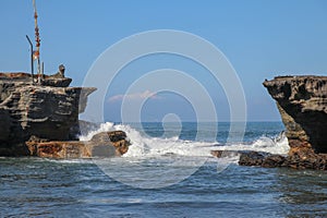 Wave crashing onshore at low tide in Bali, Indonesia. Water cascading over stone, feeding tidal pool. Wave breaking on rock during