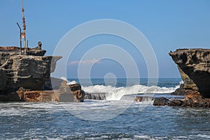 Wave crashing onshore at low tide in Bali, Indonesia. Water cascading over stone, feeding tidal pool. Wave breaking on rock during