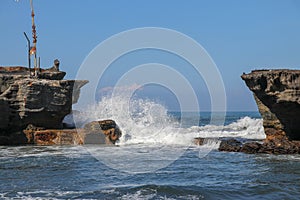 Wave crashing onshore at low tide in Bali, Indonesia. Water cascading over stone, feeding tidal pool. Wave breaking on rock during