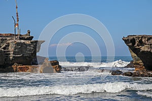 Wave crashing onshore at low tide in Bali, Indonesia. Water cascading over stone, feeding tidal pool. Wave breaking on rock during