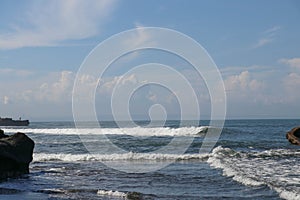 Wave crashing onshore at low tide in Bali, Indonesia. Water cascading over stone, feeding tidal pool. Wave breaking on rock during