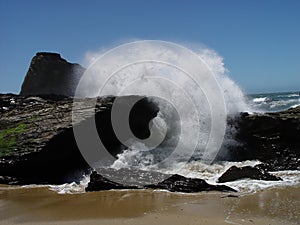 Wave Crashing Over Rocks On Sandy Beach Blue Sky