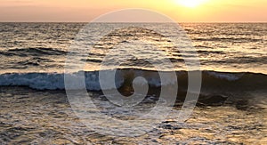 Wave crashing in the sea, at sunset with water drops splashing and flying in the air and warm orange color from the sun