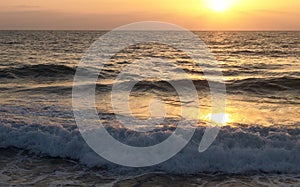 Wave crashing in the sea, at sunset with water drops splashing and flying in the air and warm orange color from the sun