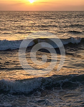 Wave crashing in the sea, at sunset with water drops splashing and flying in the air and warm orange color from the sun