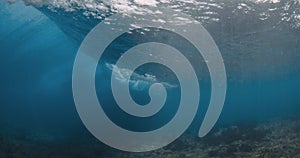 Wave crashing in transparent blue ocean. Underwater view of powerful barrel wave with foam