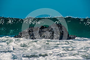 Wave cresting behind rock in foamy seas