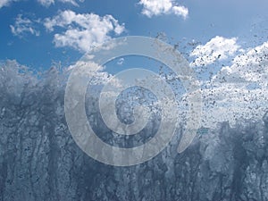 Wave explodes into the air with blue cloud sky in the background