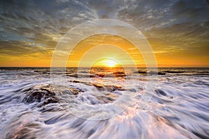 The wave flows over weathered rocks and boulders at North Narrabeen