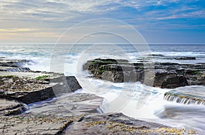 The wave flows over weathered rocks and boulders at North Narrabeen