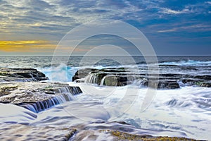 The wave flows over weathered rocks and boulders at North Narrabeen
