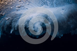 Wave with foam and bubbles crash in ocean. Underwater view of ocean wave