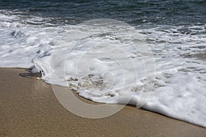 Wave with foam on sandy Mediterranean beach. Close up view. Natural texture background