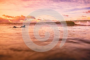 Wave in ocean at bright sunset or sunrise with surfer. Wave with warm sunrise colors