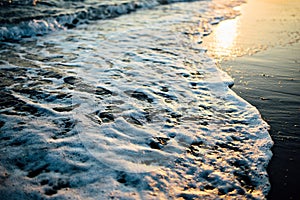Wave of the ocean sea on the sand beach at the sunset light. photo