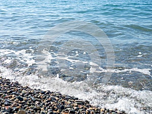 Wave on a pebbly shore. Sea foam. Bathing place. Nature of the south. Close-up of the coastline