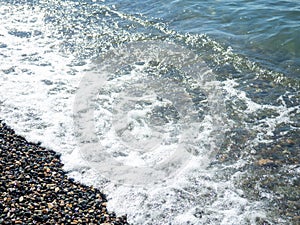 Wave on a pebbly shore. Sea foam. Bathing place. Nature of the south. Close-up of the coastline