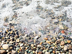 Wave on a pebbly shore. Sea foam. Beautiful pebble beach. Close-up of the coastline