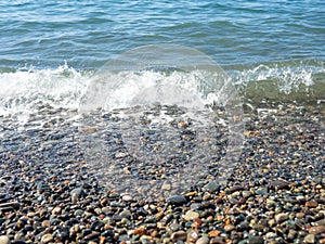 Wave on a pebbly shore. Sea foam. Beautiful pebble beach. Close-up of the coastline