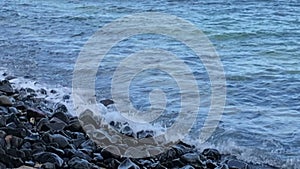 Wave rushing toward pebble stone beach.Slowmotion close up on stones in the beach. Footage. Sea waves at the shore in a