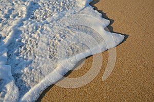 Wave of the sea entering the sand of the beach forming foam, contrast of white and beige. Macro photography