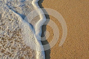 Wave of the sea entering the sand of the beach forming foam, contrast of white and beige. Macro photography