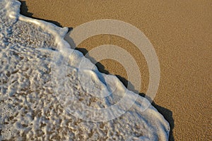 Wave of the sea entering the sand of the beach forming foam, contrast of white and beige. Macro photography