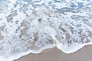 Wave of the sea on sandy beach white foam.Top view of a wave breaking on the sand at the beach. Top view,Copy space