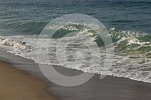 Wave swell rising up at edge of washback foam, with bacspray, on snady shore