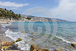 Waves against rock and, in the background, the italian coast with the town of Arma di Taggia