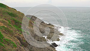 Waves on the azure water in the tropical sea. An island with a rocky shore and green plants