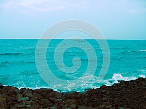 Waves of a blue sea crashing into the rocks at the beach in Puducherry, India.