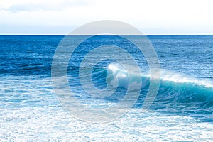 Waves braking close to the beach shore with blue turquoise ocean water and resulting white foam