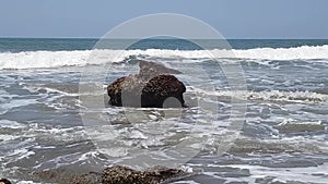 Waves break against huge rock in sea near shore.